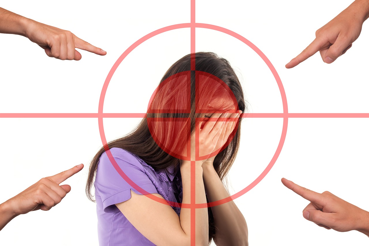 A woman covering her face with her hands in shame while fingers point from every direction.